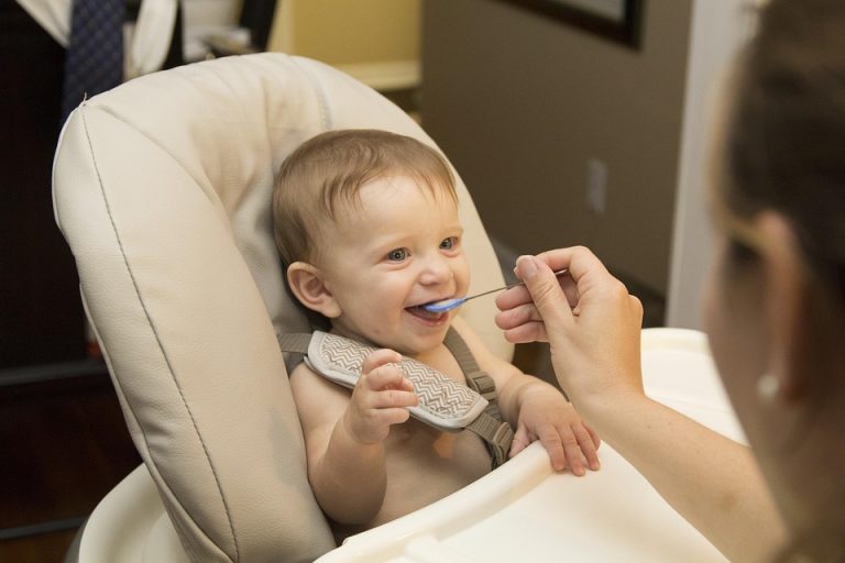 Parent spoon-feeding a smiling baby in a high chair