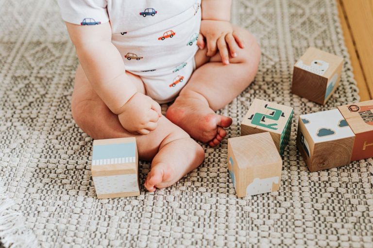Baby sitting on a rug playing with wooden toy blocks