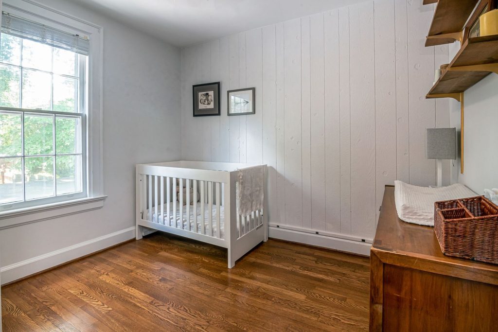 Empty white wooden crib with a fitted mattress in a bright room