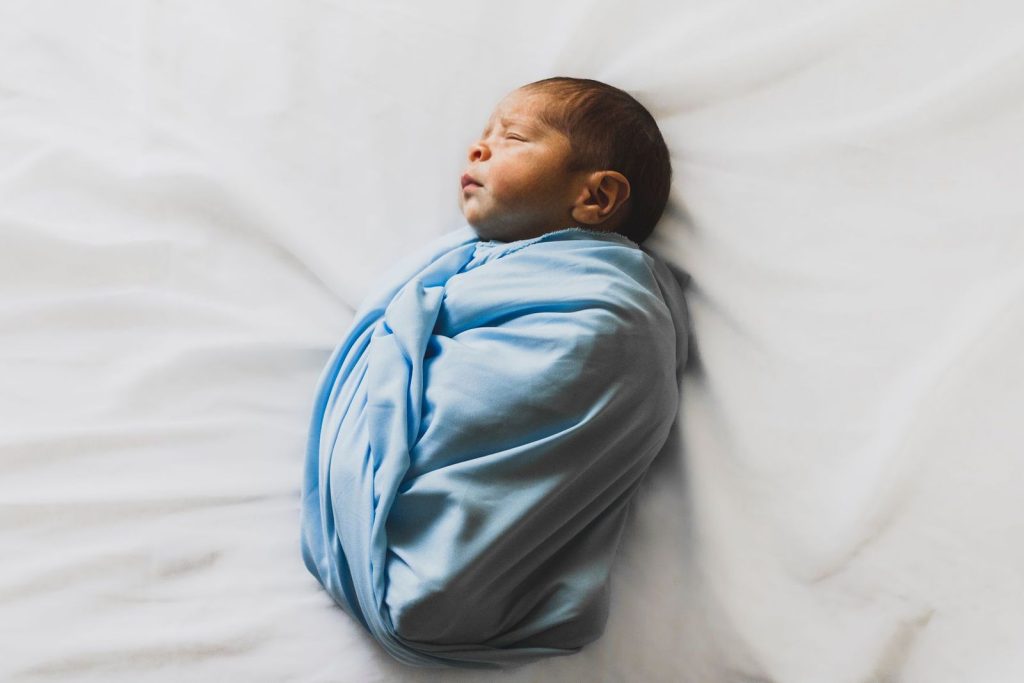 Swaddled newborn baby lying on their back on a white sheet