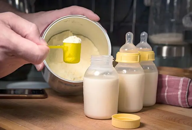 Parent measuring powdered infant formula next to prepared bottles