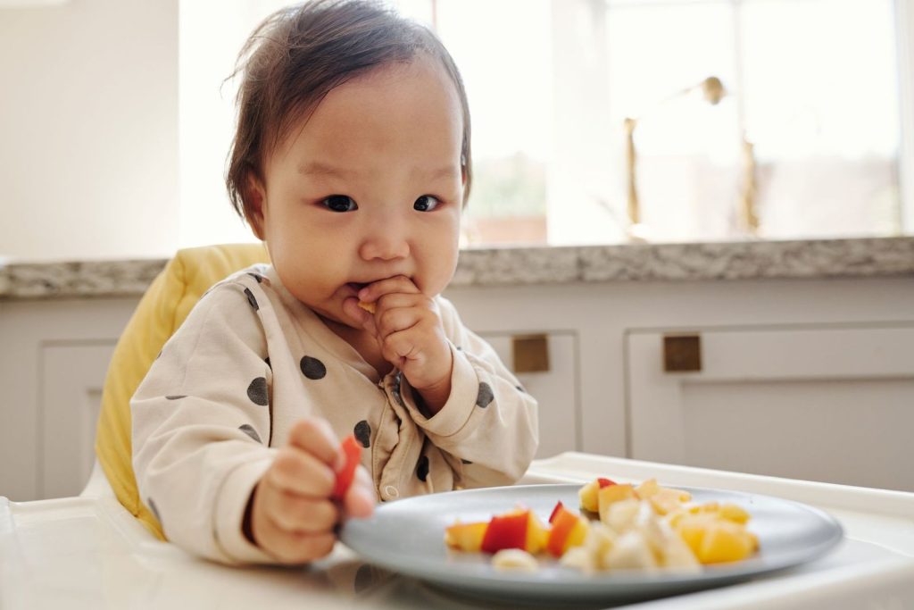 Baby in a high chair eating fresh fruit