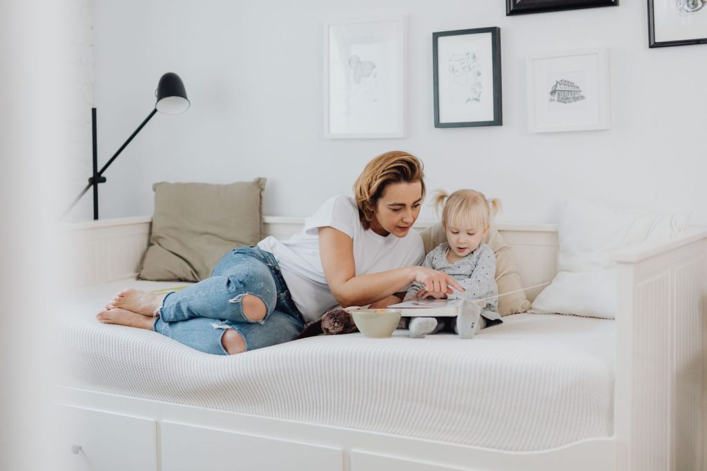 Mother and toddler reading a book together on a low bed