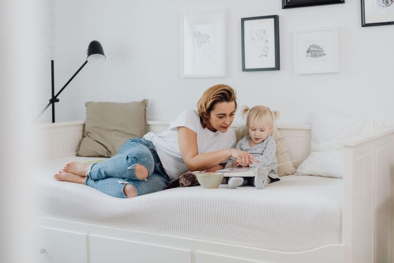 Mother and toddler reading a book together on a low bed