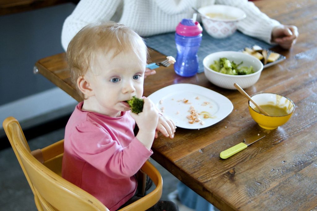 Toddler eating vegetables at the family table
